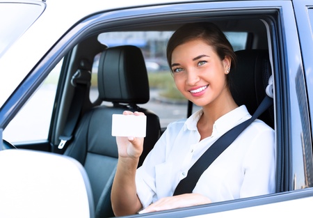 Happy girl in a car showing an empty white card for your messageの写真素材
