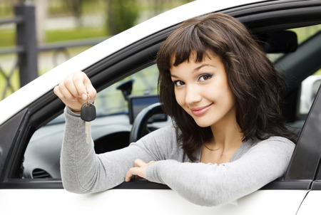 Pretty female driver in a white car showing the car keyの写真素材