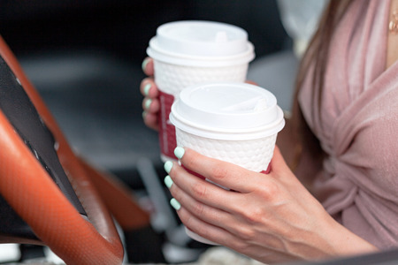 Closeup shot of hands of female driver who holds two paper cups with tea or coffeeの写真素材