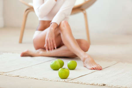 Woman with long legs sitting on the floor with green apples. Focus is located on the nearest apple. Healthy nutrition conceptの写真素材