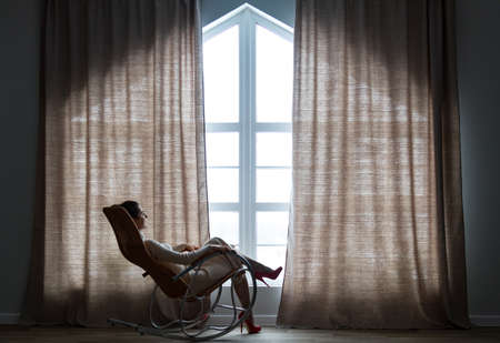 Woman sitting in a rocking chair and looking in a windowの写真素材