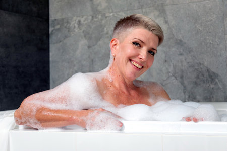 Beautiful middle-aged woman relaxing in a bathtub with foam