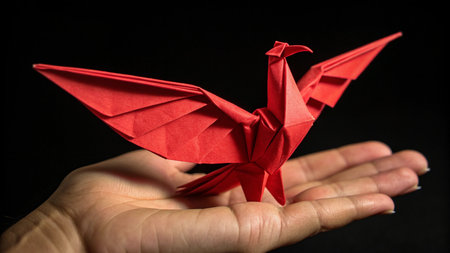 Red origami crane in hand on a black background. Close upの素材