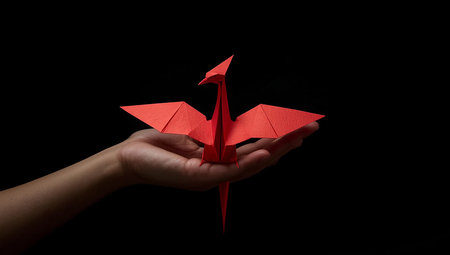 Hand holding origami red paper bird on black background, business conceptの素材