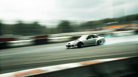 a silver sports car drifting on a racetrack with tire smoke and blurred background showing high speed and control in an outdoor racing facilityの素材