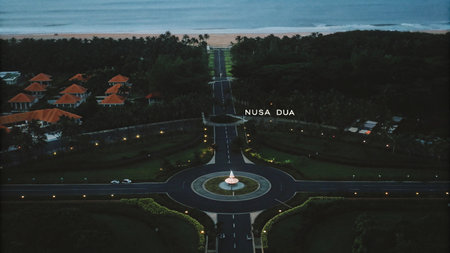 Experience the tranquil beauty of Nusa Dua, Bali at dusk. This aerial view showcases a meticulously planned tropical avenue, lush greenery, and illuminated resort areas, creating a serene and inviting evening scene for travelers.の素材