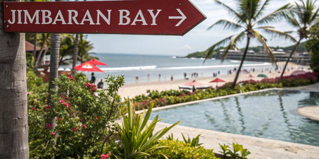 A tropical sign points towards a beautiful bay beach. Enjoy the relaxing view of the sand, sea, and pool in this idyllic paradise, perfect for a sunny vacation.の素材