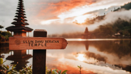 A descriptive signpost marks the entrance to Ulun Danu Beratan Temple, a beautiful Balinese Hindu temple nestled by Lake Beratan amidst misty mountains, reflecting the tranquil morning light.の素材