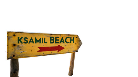 A weathered rustic yellow sign with green lettering and a red arrow points the way to Ksamil Beach. This sun-drenched sign evokes a sense of travel, adventure, and relaxation, guiding visitors to a beautiful coastal destination.の素材