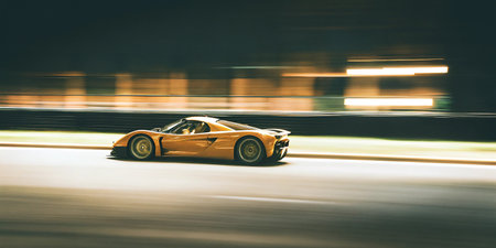 A powerful golden performance vehicle speeds along a dark road at night. This dynamic image captures the thrill of motion with beautiful blur effects, highlighting sleek lines and intense speed.の素材
