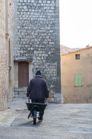 Rural scene in the south of France in Provence, an old man in a medieval village pulling a...
