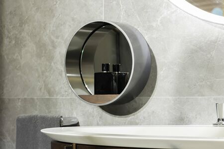 Detail on the round mirror of a modern steel bathroom with a bottle of perfume for men