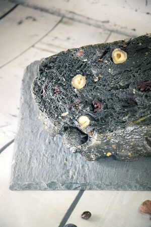 Closeup on a black bread with charcoal cereals and dried fruits set on a white bread slices on a wooden kitchen splashbackの写真素材