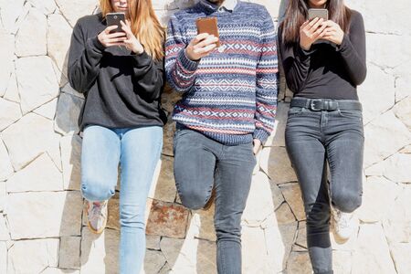 Young people using their smartphone against a wall cut face unidentified personの写真素材