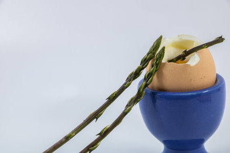 Eggs with asparagus in blue egg cup on white background
