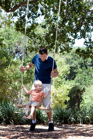 father and smiling happy son on a swing の写真素材