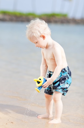 cute toddler using watering pot on a beachの写真素材
