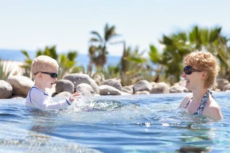 cheerful mother and her son splashing in the pool