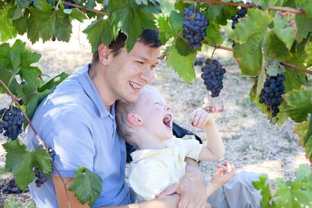 handsome father and his son eating grapes at a vineyardの写真素材