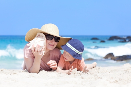 mother is lying with her son at a tropical beach and listening to a shellの写真素材