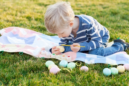 adorable little boy coloring easter eggs in the parkの写真素材