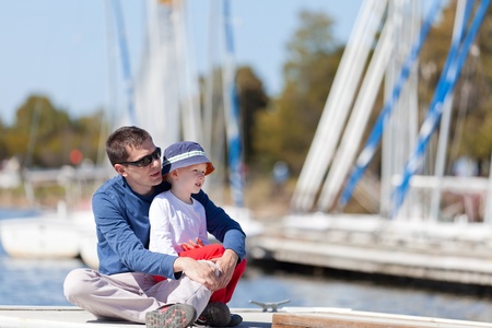 caucasian father and his son sitting at a marina dock togetherの写真素材