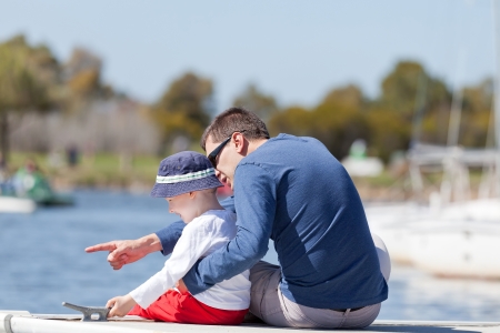caucasian father and his son sitting at a marina dock togetherの写真素材