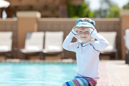 cute smiling caucasian boy sitting by the pool and enjoying summer vacationの写真素材