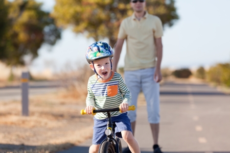 excited caucasian boy riding a balance bike and his father waitingの写真素材