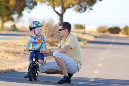 happy laughing son at the balance bike and his handsome father spending fun time together at the parkの写真素材