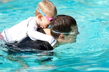 laughing cute son playing and swimming with his handsome young father at the poolの写真素材