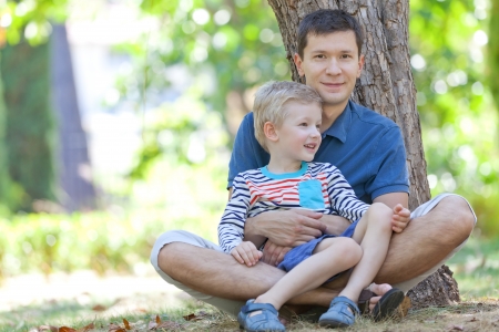 handsome smiling father and his cute son sitting together in the woodsの写真素材