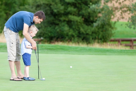 handsome young father teaching his cute son to play golfの写真素材