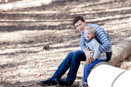 handsome young man and his cute smiling son sitting together on a tree log during the hike in the woodsの写真素材