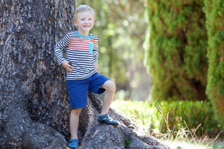 cute positive smiling boy standing at the tree rootsの写真素材