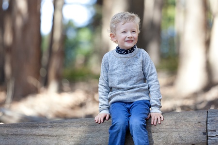 happy laughing positive boy sitting on a tree log in the woods during the hikeの写真素材