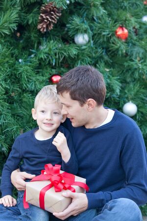 happy family of young father and cute son with present by the christmas treeの写真素材