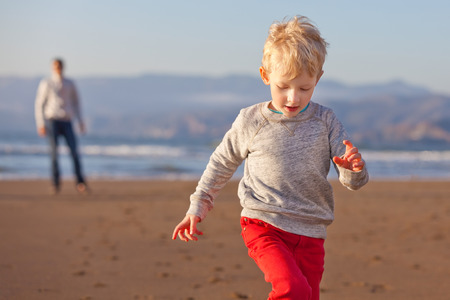 positive cheerful son running away from his father at the beach in californiaの写真素材