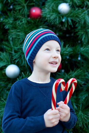 cute cheerful boy with candy canes by the christmas treeの写真素材