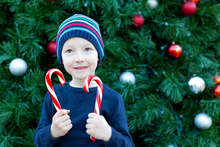 cute cheerful boy with candy canes by the christmas treeの写真素材