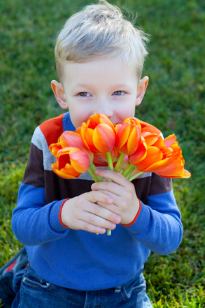 positive smiling boy holding beautiful flowers at spring timeの写真素材
