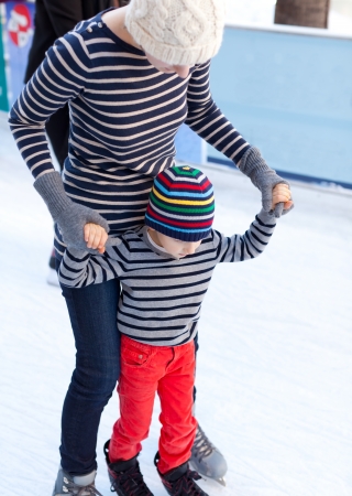 cheerful mother and her little son enjoying ice skating together at winterの写真素材