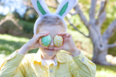 cute smiling boy with bunny ears holding bright easter eggs at spring time