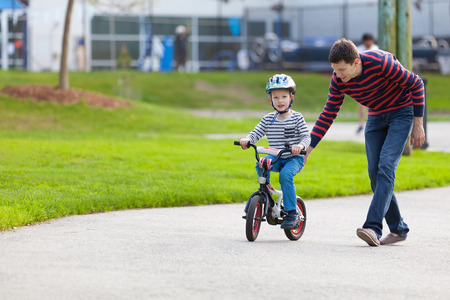 young father teaching his smiling son how to ride a bikeの写真素材