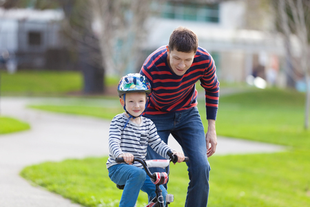 young father teaching his smiling son how to ride a bikeの写真素材
