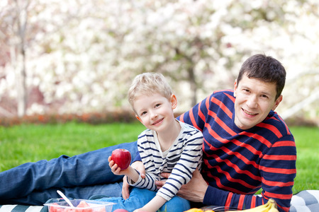 family of father and son having picnic together, little son holding red appleの写真素材