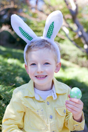 cheerful smiling little boy in bunny ears holding easter egg at spring timeの写真素材