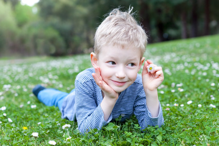 cute smiling boy lying at grass with flowers and dreaming at summer timeの写真素材