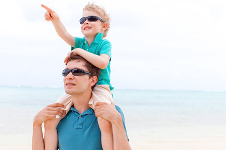 little boy sitting at his father shoulders at pointing at something with his fingerの写真素材