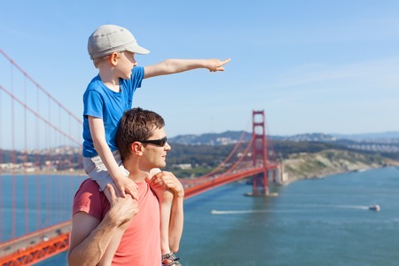 little son sitting at his father shoulders and enjoying together the view of golden gate bridge in san francisco, californiaの写真素材